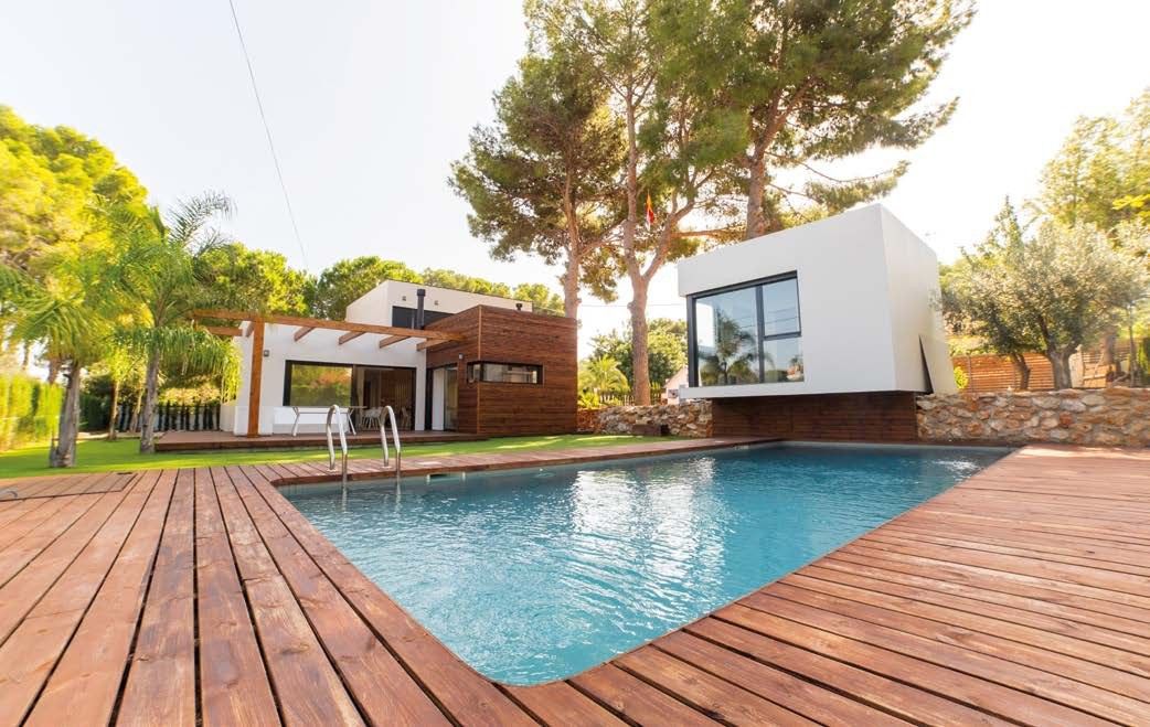Casa modular en Dénia con un volumen blanco junto a la piscina, cuerpo revestido de madera, pérgola y pinos