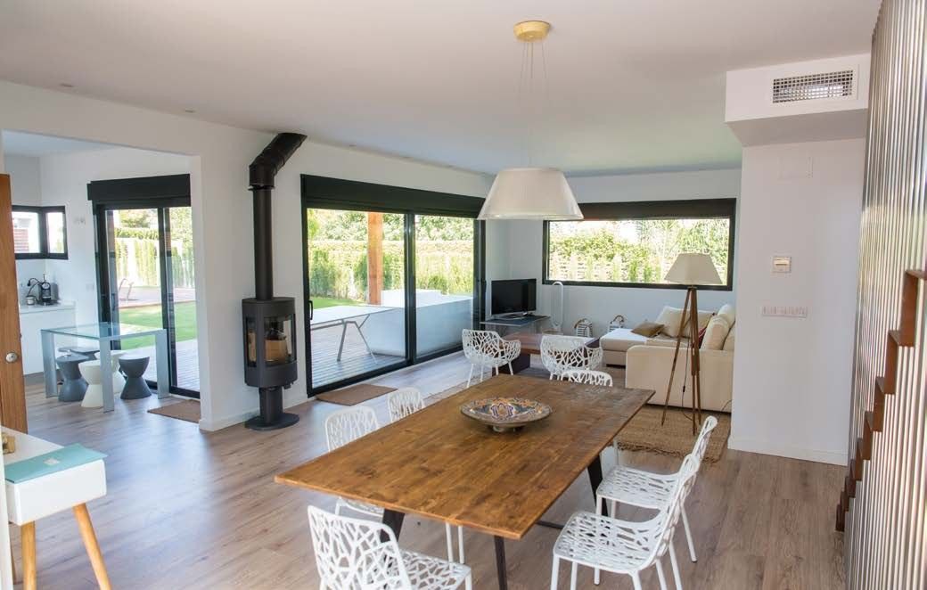 Salón comedor diáfano con estufa de leña, suelo de madera y ventanales corredizos abiertos a la terraza