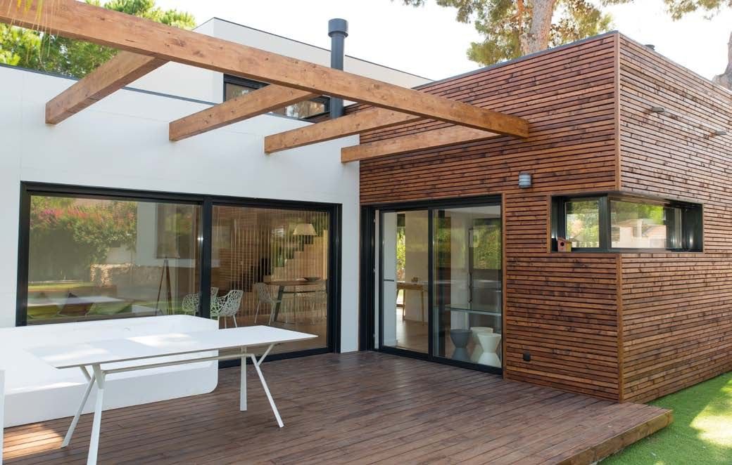 Terraza de tarima bajo una pérgola de vigas de madera, junto al volumen revestido de lamas horizontales