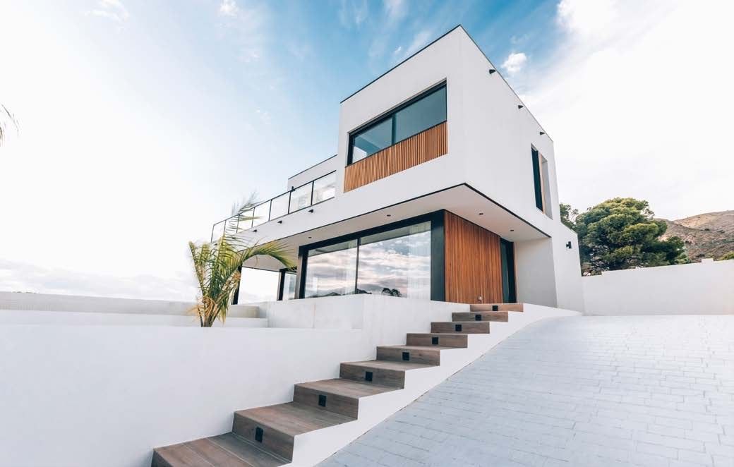 Casa modular en Finestrat vista desde el acceso: volumen blanco volado con lamas de madera y escalera exterior de peldaños de madera
